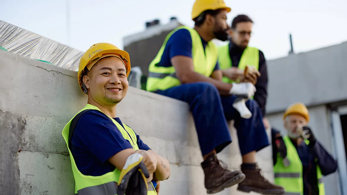 Team of construction workers in bright safety vests and helmets taking a break together outdoors.