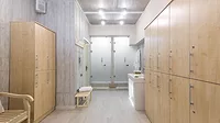 Feature image of a locker room Feature image of a locker room with wooden lockers, a robe, hand towels in a basket and two showers in the back.