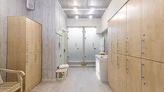 Feature image of a locker room with wooden lockers, a robe, hand towels in a basket and two showers in the back.