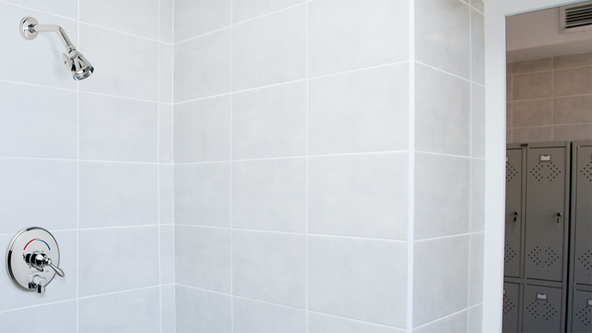 A close-up of a white-tiled shower that shows the shower head and shower controls.