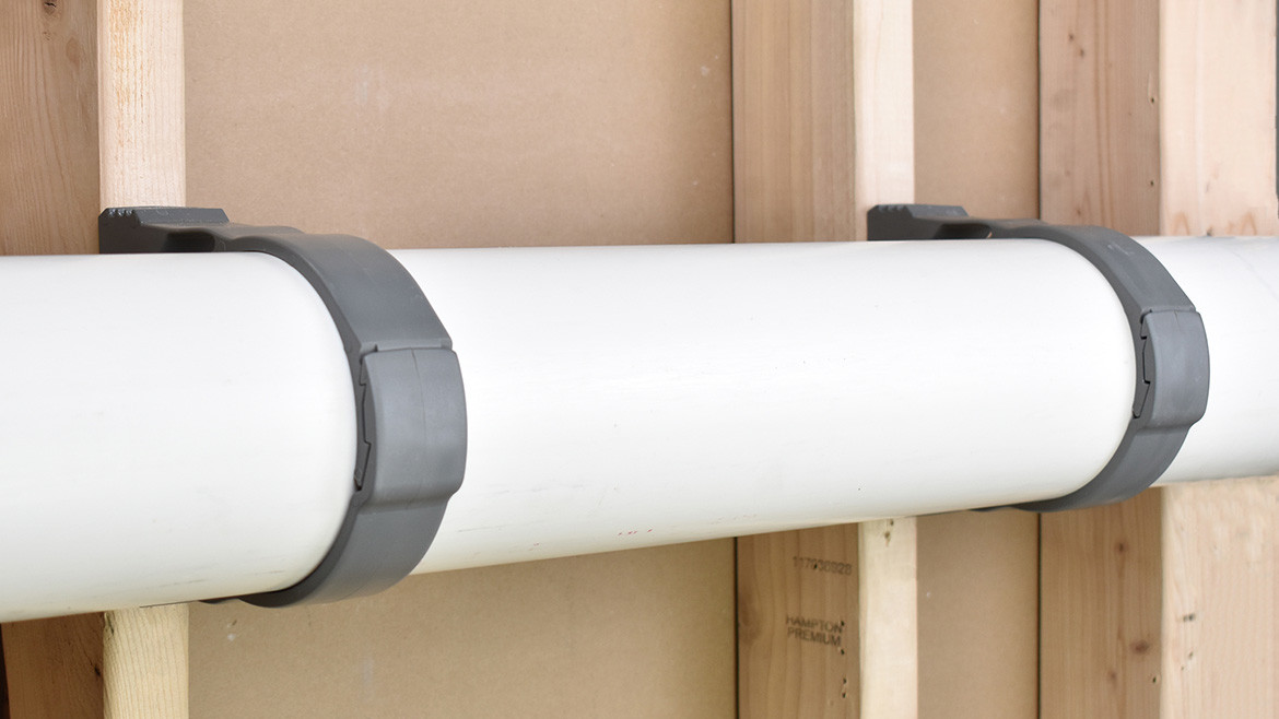 Two gray pipe supports supporting white piping along a wall.