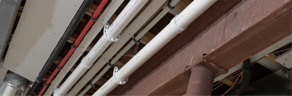 Twp white pipes with white pipe supports along a ceiling with other plumbing, HVAC, and mechanical systems.