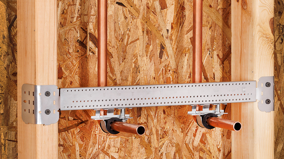 Two copper pipes with pipe supports along the inside of a wall.