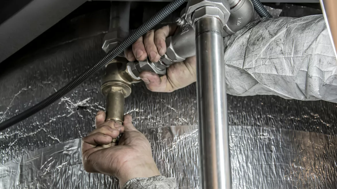 Plumber's hands with dirty sleeves, gripping pipes to turn it, a silver thermal material in the background.
